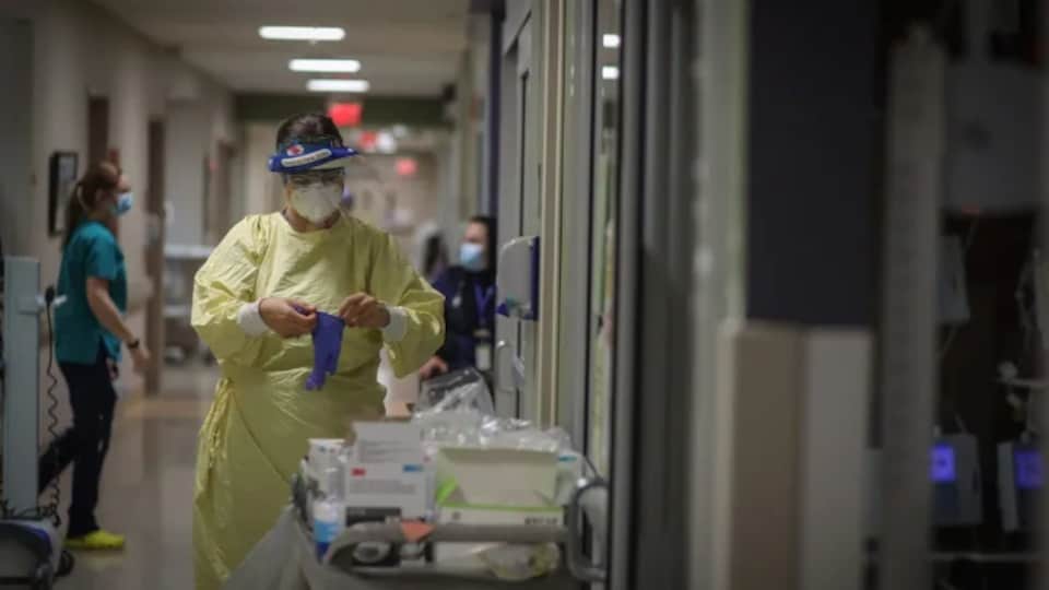 Un professionnel de la santé dans un couloir d'hôpital en train de mettre des gants.
