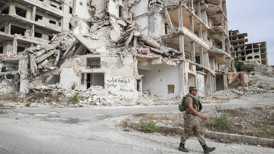 Un soldat marche devant un immeuble en ruines.
