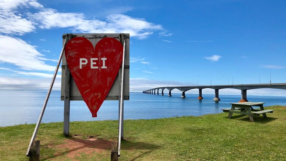 Une affiche en forme de coeur où sont inscrites les lettres « PEI », devant le pont de la Confédération.