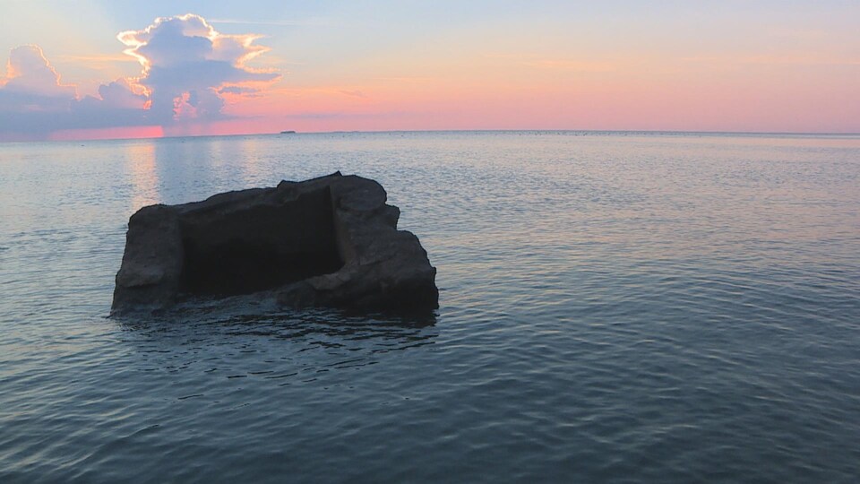 Une pierre au milieu de l'eau avec un ciel dégradé par le coucher du soleil.
