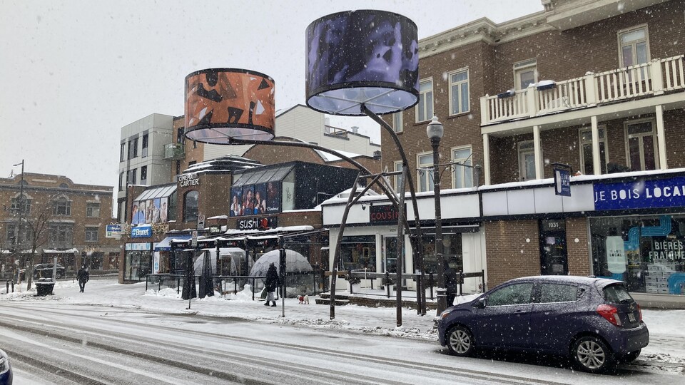 Plan large de l'avenue Cartier en hiver, bordée de grands lampadaires. Il y a de la neige au sol et le ciel est nuageux.