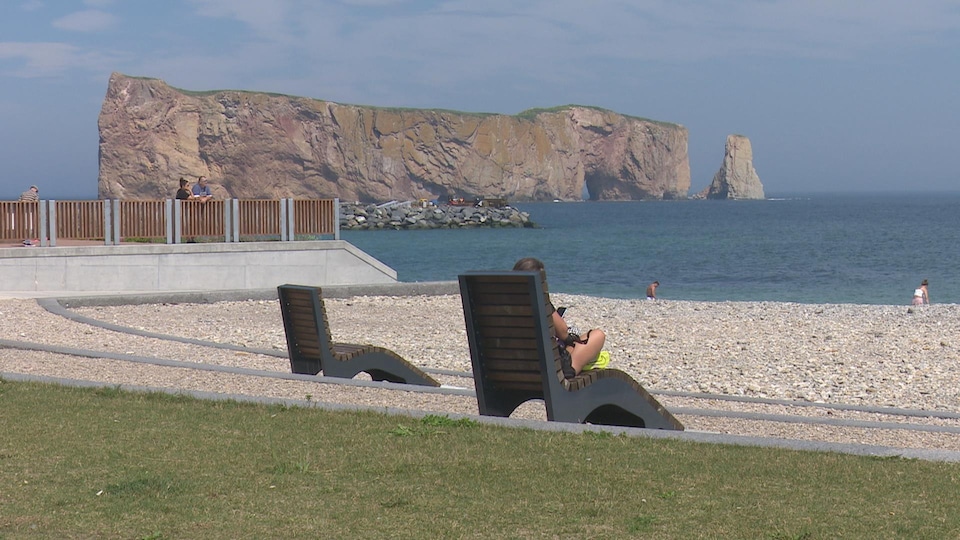 Une femme est assise sur une chaise longue sur une plage devant le Rocher Percé.