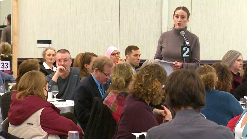 Heather Hollett parle à un micro au milieu d'une foule assise à des tables dans une salle de conférence.
