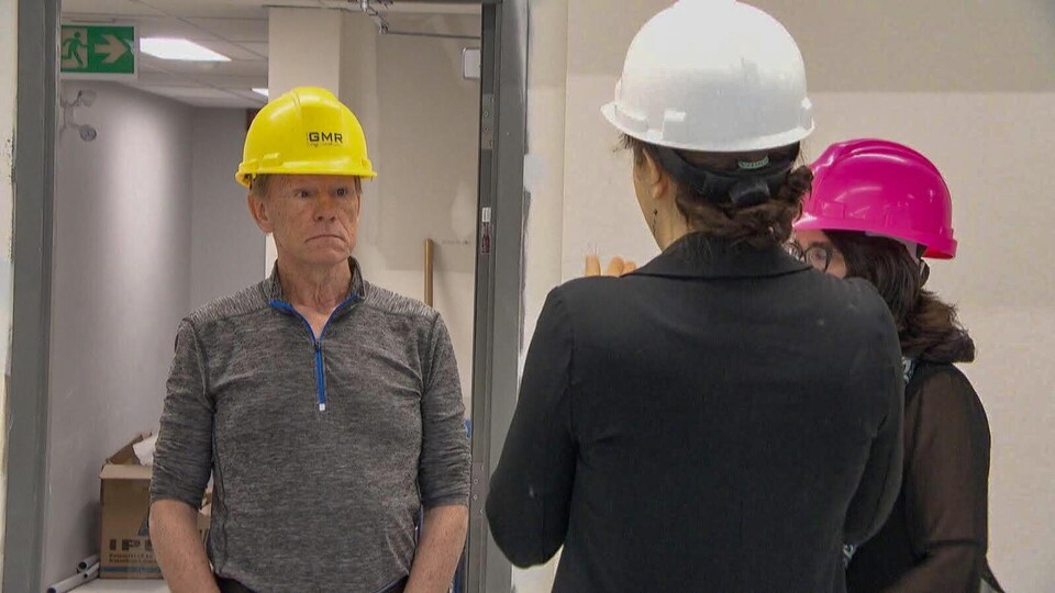 Un homme et deux femmes portent des casques de construction.