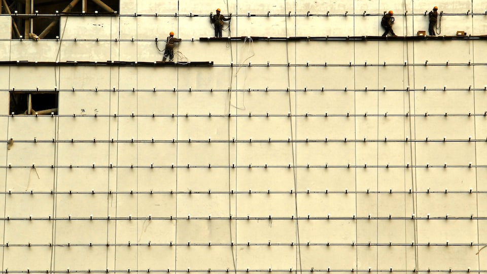 Des travailleurs sont debout sur des planches de bois à l'avant d'un bâtiment en construction dans le centre de Pékin, le 13 février 2012.