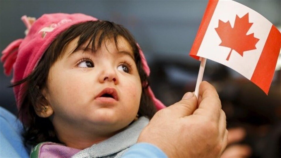 Une jeune réfugiée syrienne regarde un petit drapeau du Canada.