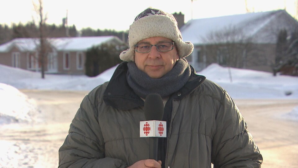Un homme tenant un micro de Radio-Canada pose devant la rue en hiver
