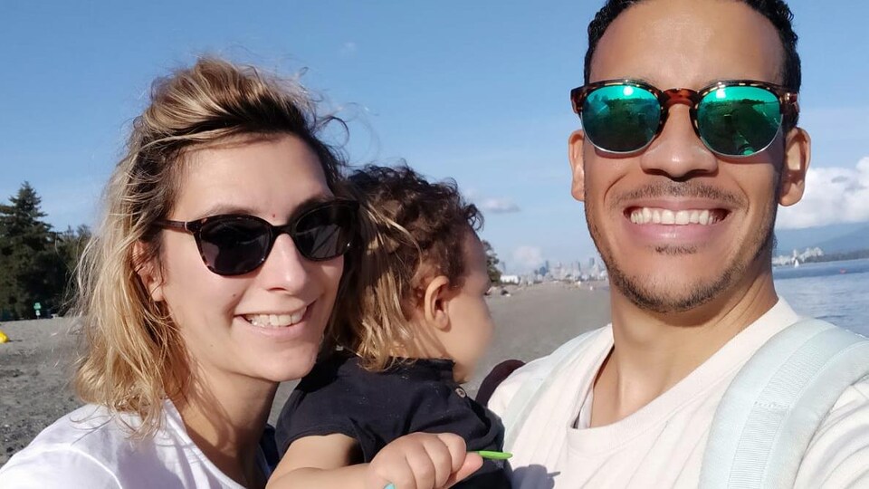 Une femme et un homme avec un bébé avec la plage derrière eux.