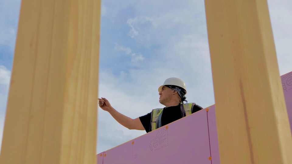 Un entrepreneur est debout sur la charpente d’une maison.