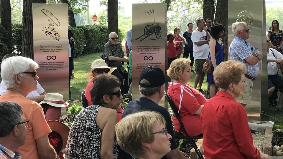 Plusieurs personnes assises dans un parc autour de plaques commémoratives aux symboles métis.
