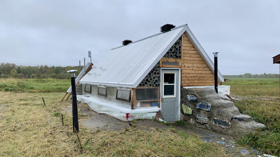 Une serre en bois et en plastique, en forme de maisonnette.