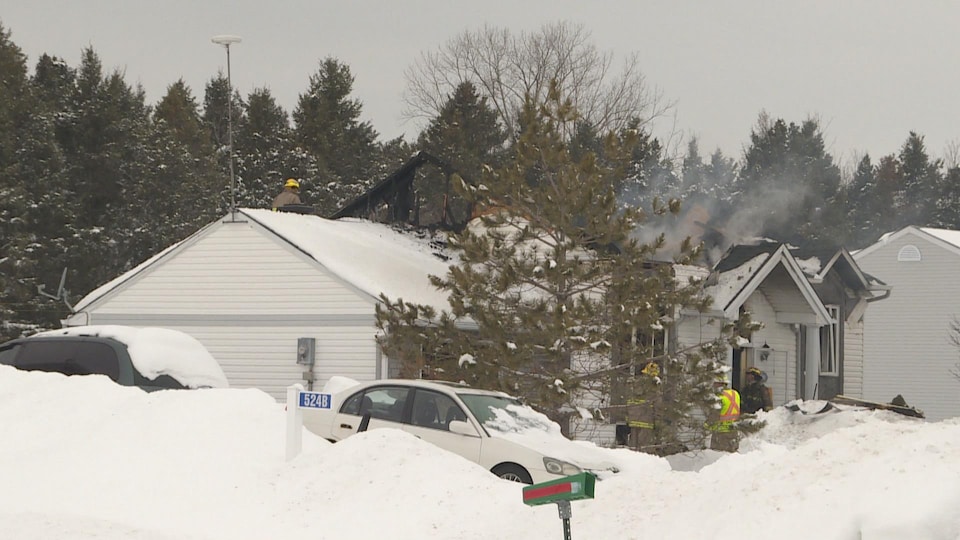 Des pompiers devant une maison endommagée par les flammes en hiver.