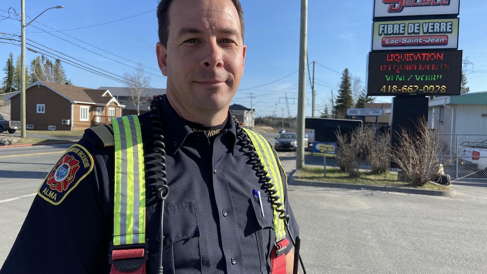 A firefighter poses in front of a sign for a business.