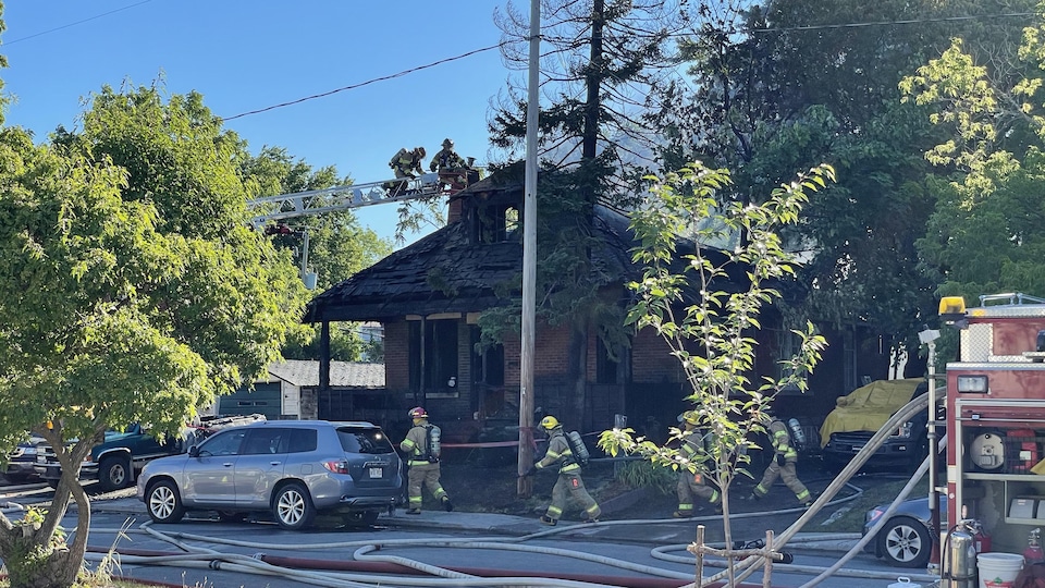 De nombreux boyaux d'incendie dans une rue devant une maison incendiée.