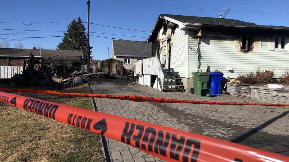 A house destroyed by fire is bounded by a banner on which is written the danger.