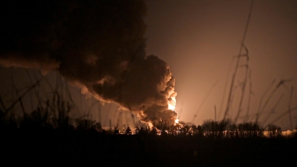 Un grand incendie brûle au loin, la nuit.