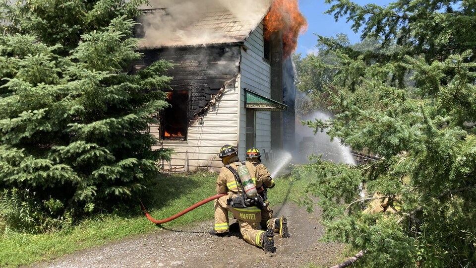 Deux pompiers luttant contre les flammes qui sortent d'une maison.