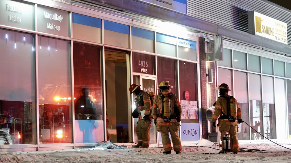 Des pompiers devant une vitrine fracassée.