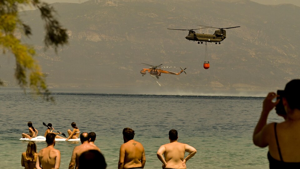 Deux hélicoptères viennent chercher de l'eau sous le regard des plaisanciers sur la plage.