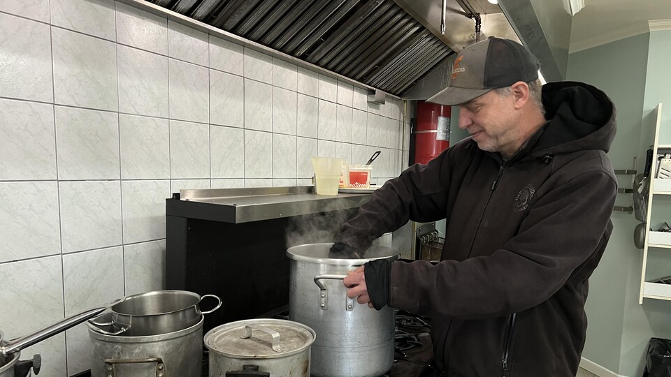 Un homme remue le contenu d'une marmite sur le rond d'une cuisinière.
