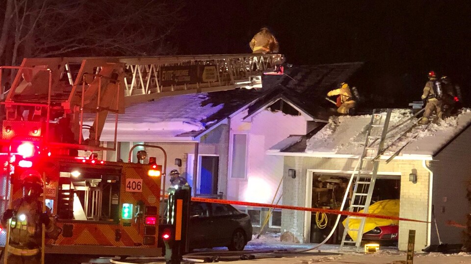 Des pompiers sont sur la toiture d'une résidence.