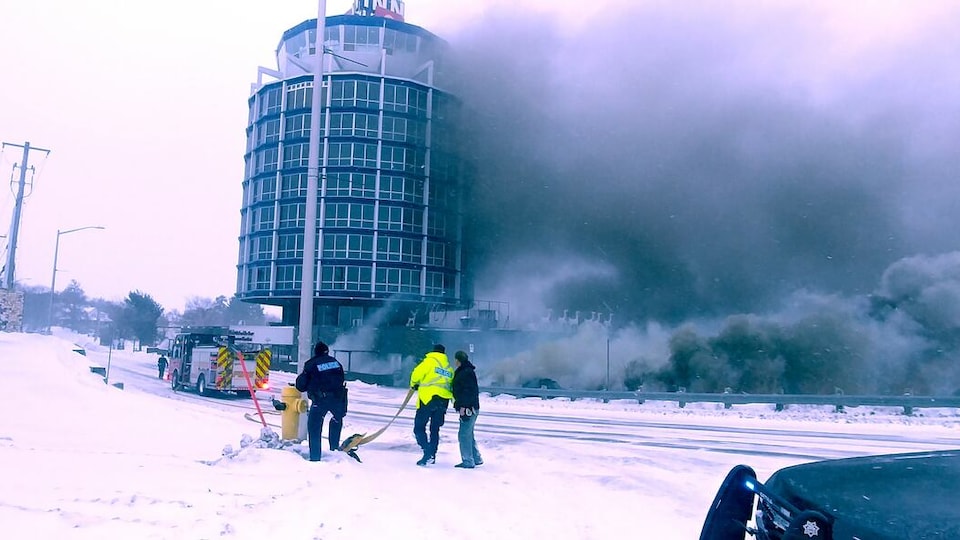Un édifice d'où s'échappe une fumée épaisse et noire. Un camion de pompier est stationné devant.
