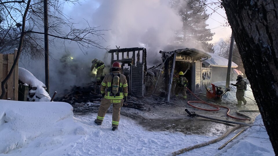 Quatre pompiers éteignent les derniers points chauds dans les décombres d'un garage.