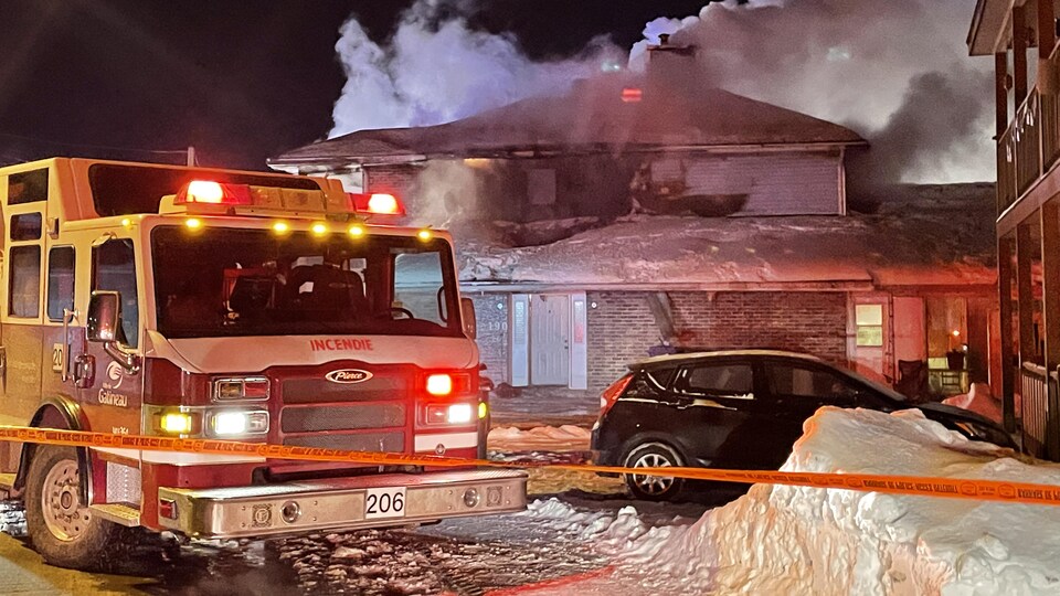 Un camion de pompiers devant une maison en flammes.