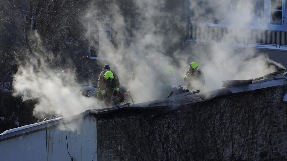Les pompiers rabattent les flammes sur le toit de l’immeuble.
