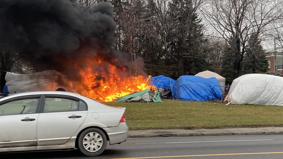 Des flammes et de la fumée noire s'échappent du campement. Une tente brûle.