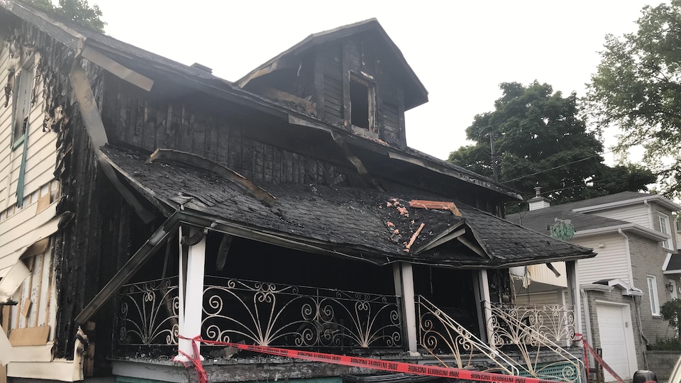 Une maison calcinée derrière un cordon rouge déployé par le service incendie.