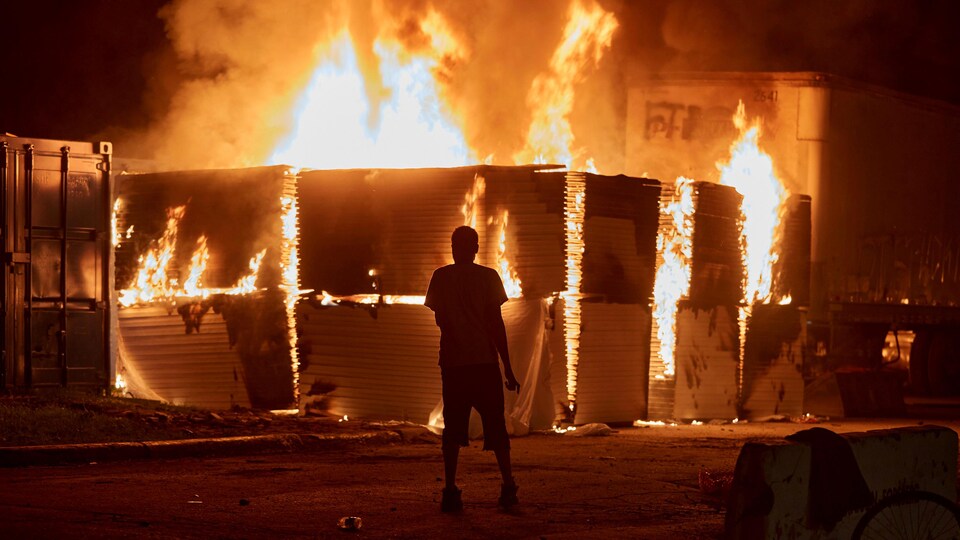 Un homme se tient face à des conteneurs incendiés.
