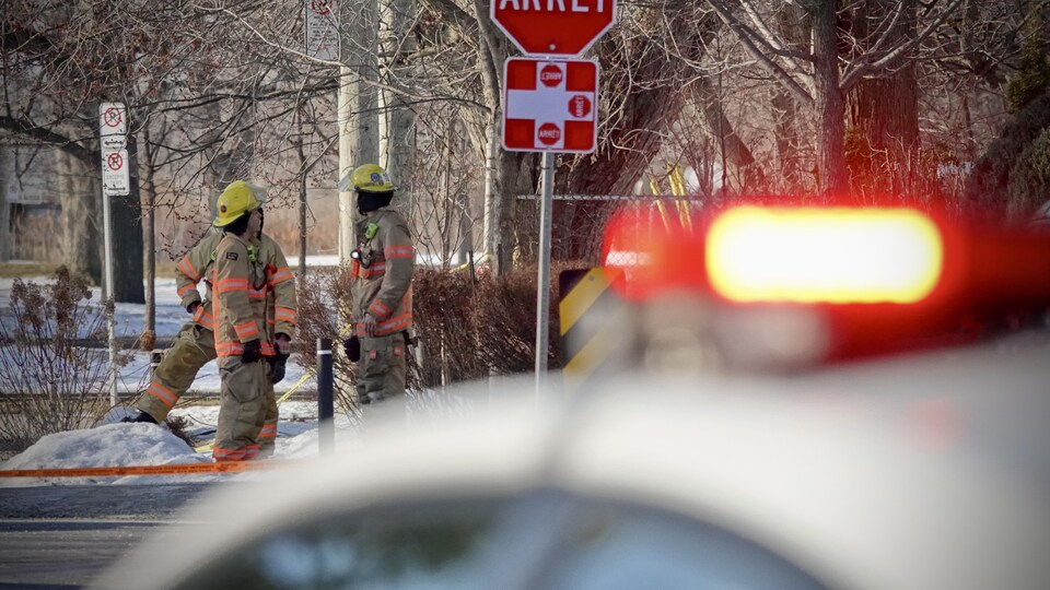 Des pompiers parlent, postés à l'angle d'une rue, alors qu'un véhicule d'urgence se trouve tout près.