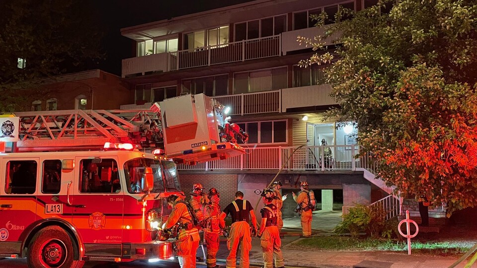 Des pompiers et un camion de pompiers devant un édifice résidentiel