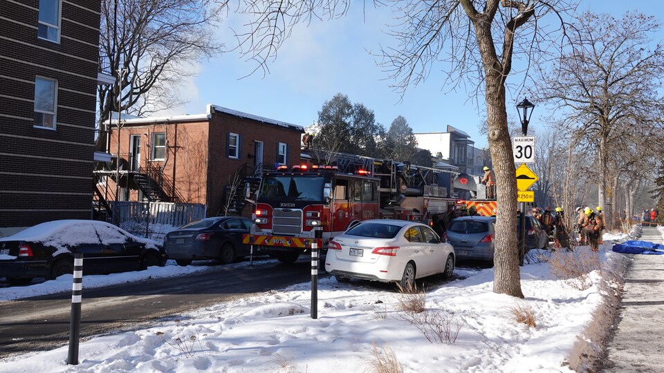 Un camion de pompiers est stationné devant l'immeuble. Un pompier se tient debout sur l'échelle du camion, qui atteint un toit.