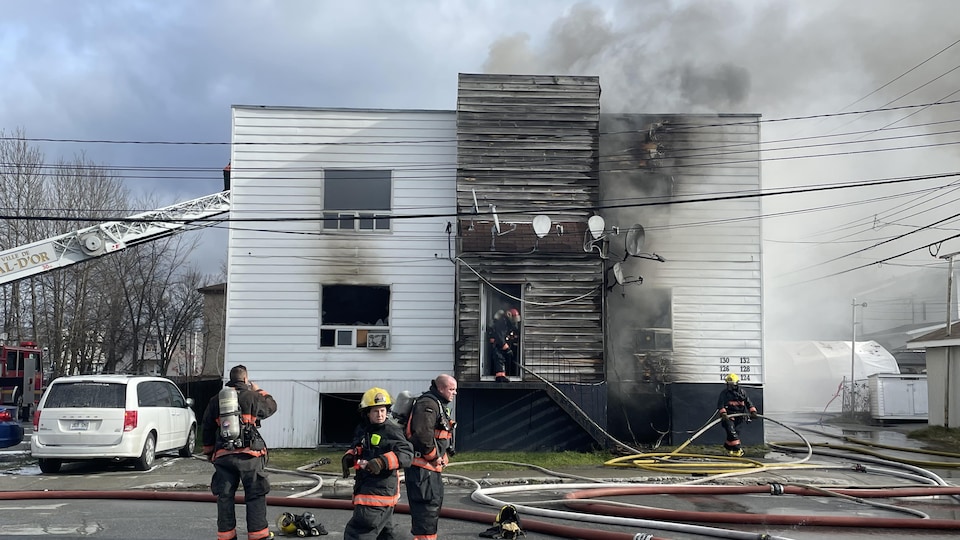 Des pompiers circulent devant l'édifice lourdement endommagé par les flammes.