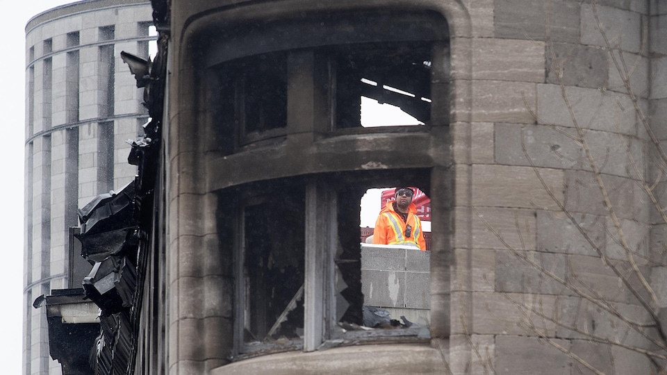 A rescue worker wearing sunglasses looks through a broken window of a minaret at a charred heritage building.