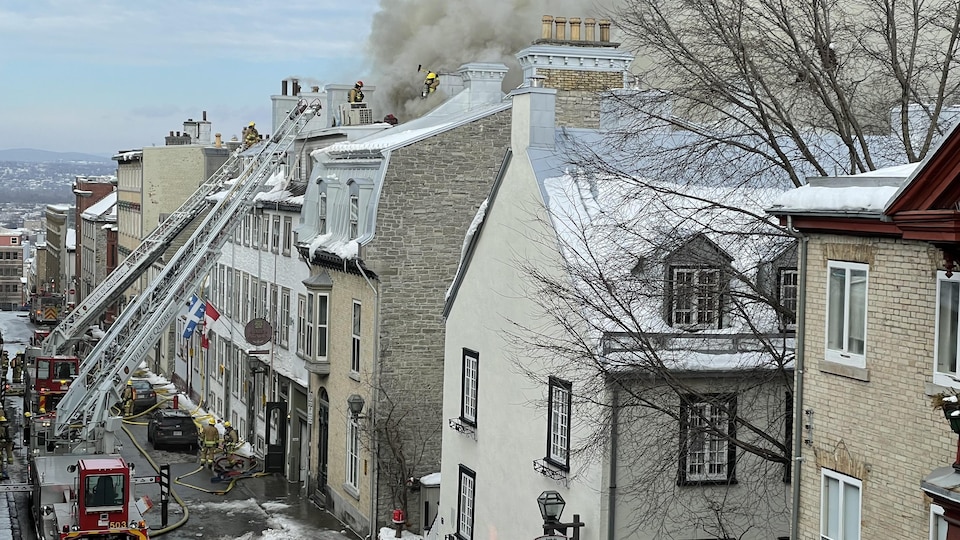 Un imposant panache de fûmée se dégage de la toiture d'un hôtel. Des pompiers sont sur place.
