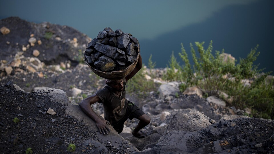 Un homme grimpe sur des rochers abruptes avec un panier rempli de charbon sur la tête.