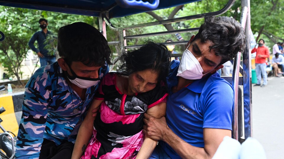 Une femme très affaiblie soutenue par deux hommes en Inde.