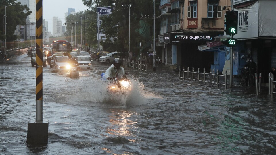 Un motocycliste roule dans une rue inondée.