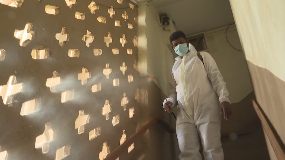 Um homem com traje de proteção desinfeta a escada com uma solução em spray.