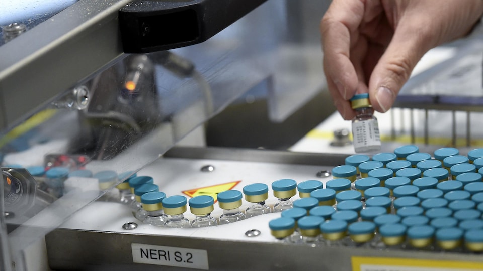 Un employé tient une fiole sur une chaîne de production dans l'usine de la multinationale pharmaceutique britannique GlaxoSmithKline (GSK).