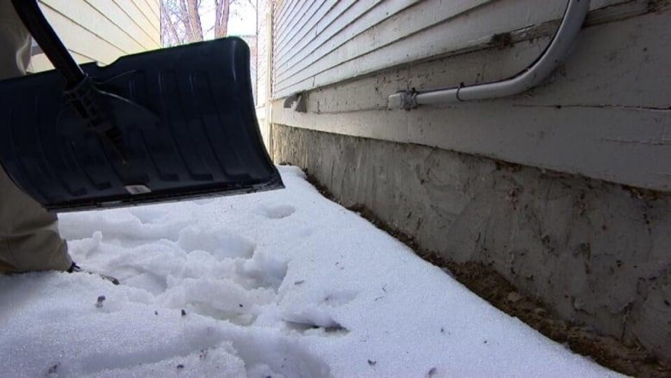 Une pelle près de la fondation d’une maison d’où l’on enlève de la neige.