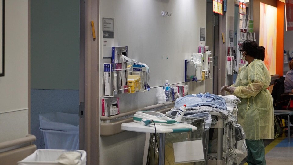 Une infirmière, vêtue d'une combinaison de protection, s'apprête à entrer dans la chambre d'un patient. 