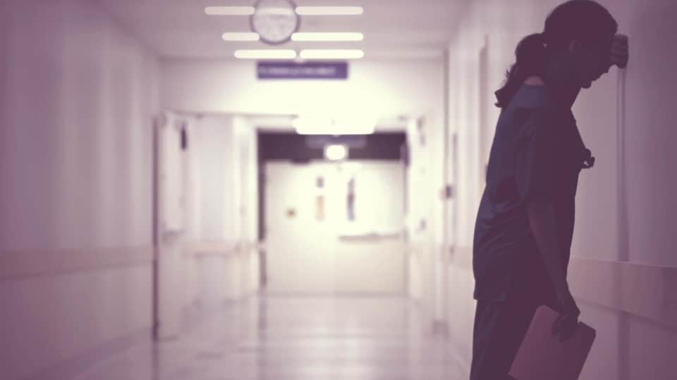 Une employée d'hôpital s'appuie sur un mur dans un corridor.