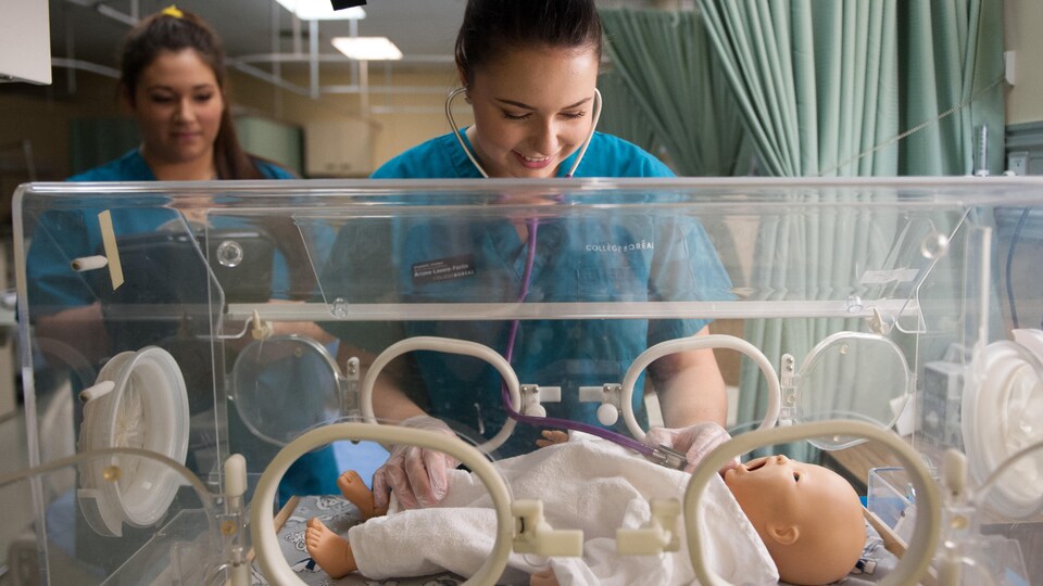 Une femme en tenue d'infirmière examine un poupon en plastique avec un stéthoscope.