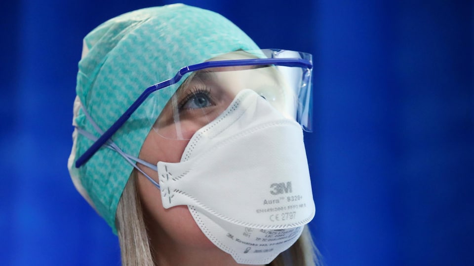 Une infirmière qui porte un masque et des lunettes de protection lève les yeux.