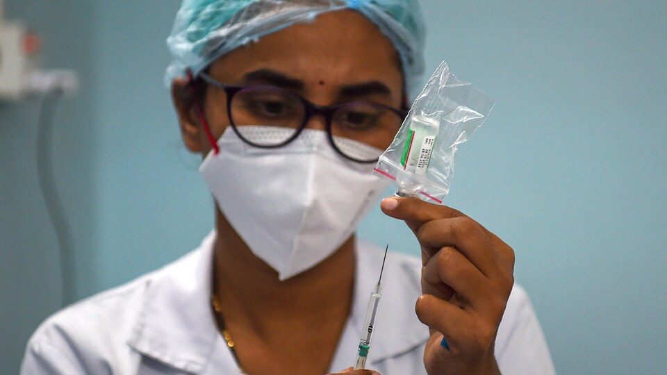 Une infirmière approche une seringue d'une fiole de vaccin.