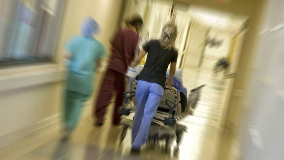 Des infirmières et la civière d'un patient le long d'un corridor d'hôpital.
